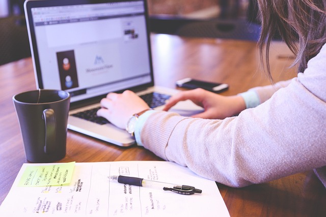 Woman sitting on laptop with coffe cup and papers next to her.