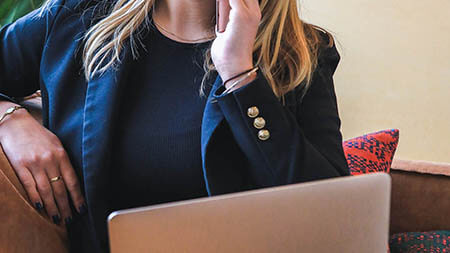 Woman sitting at laptop on her phone.