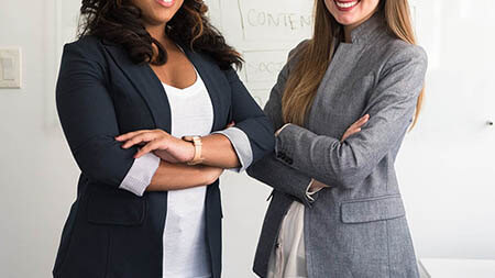 Two women dressed professionally standing in front of whiteboard.