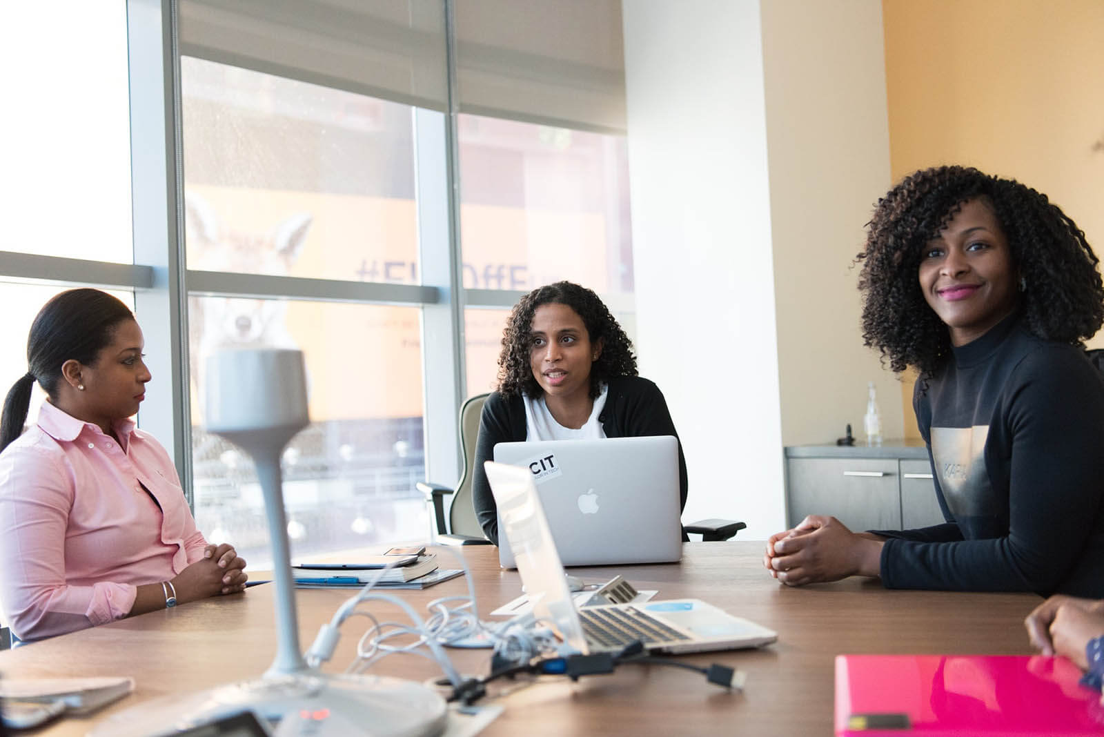 3 women sitting around a conference table with laptops open